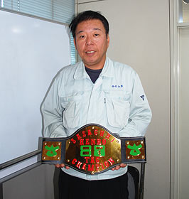 西村俊治社長と、同社が製作した、イジメ撲滅チャリティープロレスのチャンピオンベルト