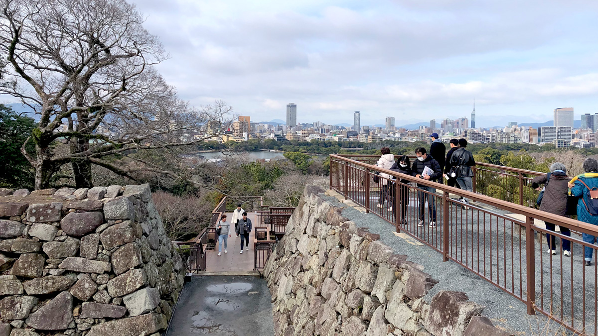 天守台の巨大な石垣と、遠景に見える福岡の都市