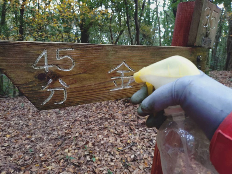 あご坂峠の道標表示板に水のスプレーをかけ汚れを落とす。ゴム手袋も100円ショップで購入